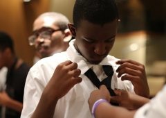 a young man receives help in tying a formal tie around a collared shirt