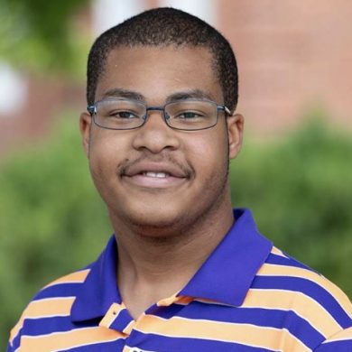 Headshot of youth leader, Jonathan, male with black hair and glasses, smiling and wearing a purple and yellow striped polo shirt