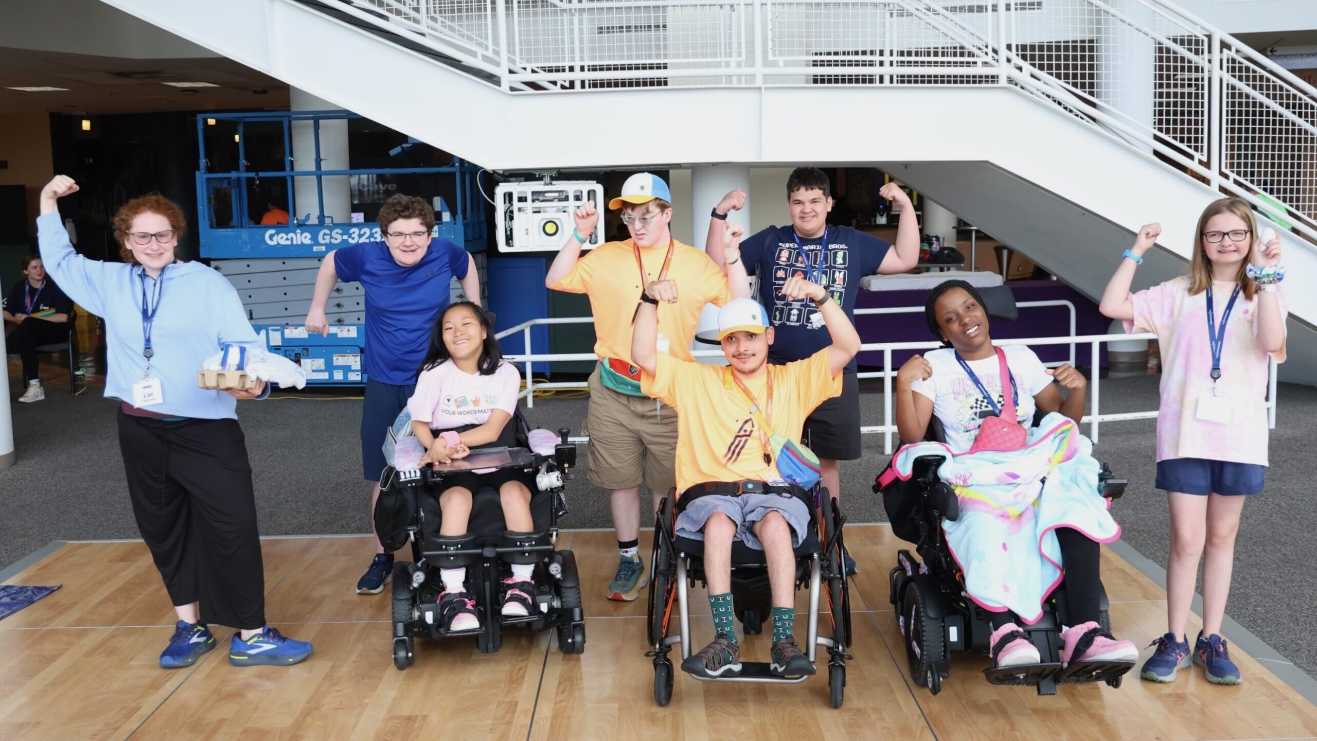 The winning team of youth from the egg drop contest at the Youth & Family Summit pose together with their arms up, flexing in victory. Five are standing and three are sitting in their motorized wheelchairs.