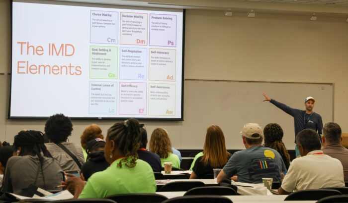 Presenter pointing to a large screen in front of a group of parents and caregivers during a family session at the 2024 Youth & Family Summit.