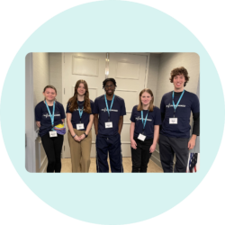 A group of five Youth Leaders standing next to each other. Everyone is wearing a navy I'm Determined t-shirt and a lanyard name tag.