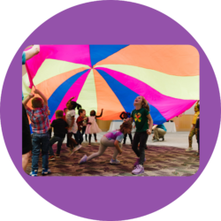 Preschool students run under a colorful parachute at an I'm Determined event.